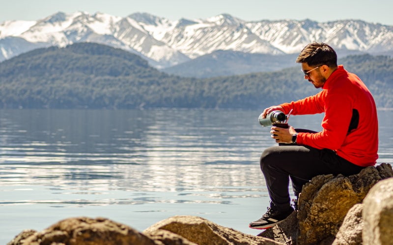 turista preparándose un mate a la orilla de un lago en la patagonia argentina