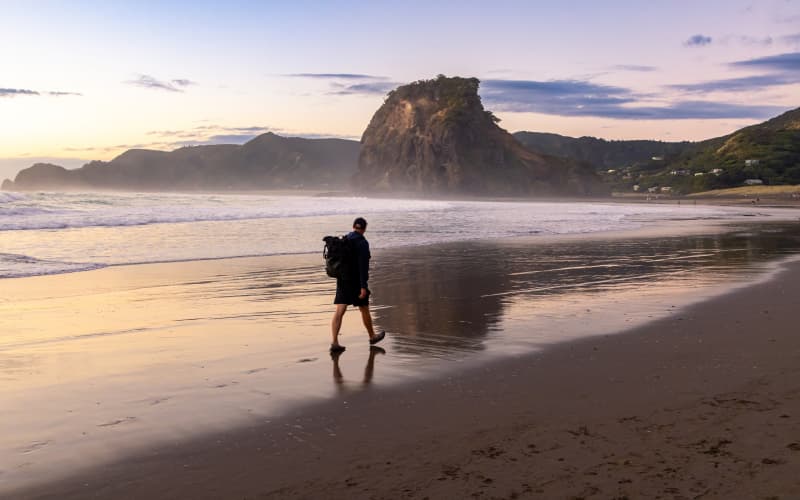 mochilero caminando por piha beach en nueva zelanda al anochecer